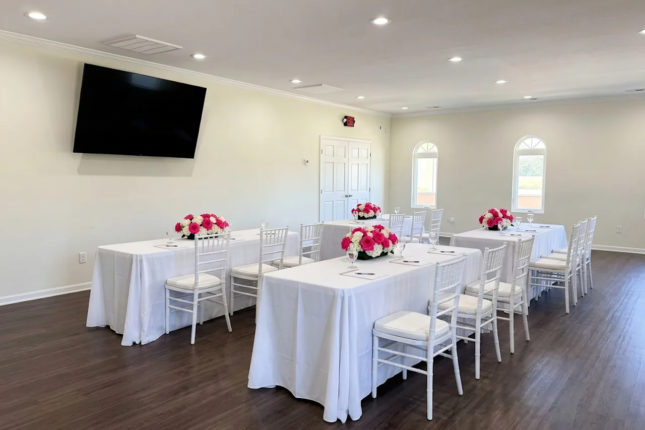 Styled concept: The Fireside Room set for a workshop, with rows of tables in white linens in the middle of the room facing the wall-mounted screen, and pink and white rose centerpieces